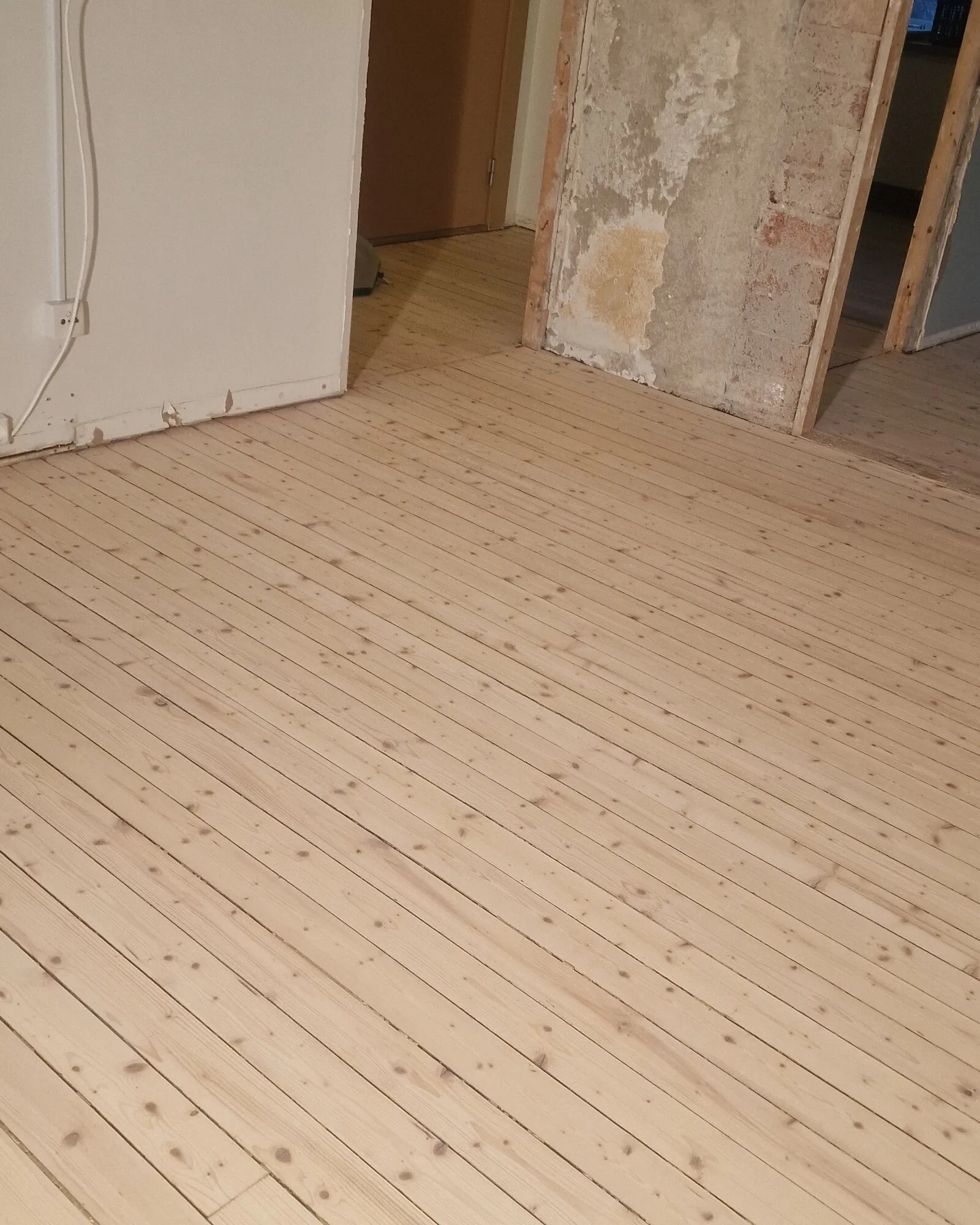 Det ferdig slipte furugulvet i rommet, med teglveggen bak