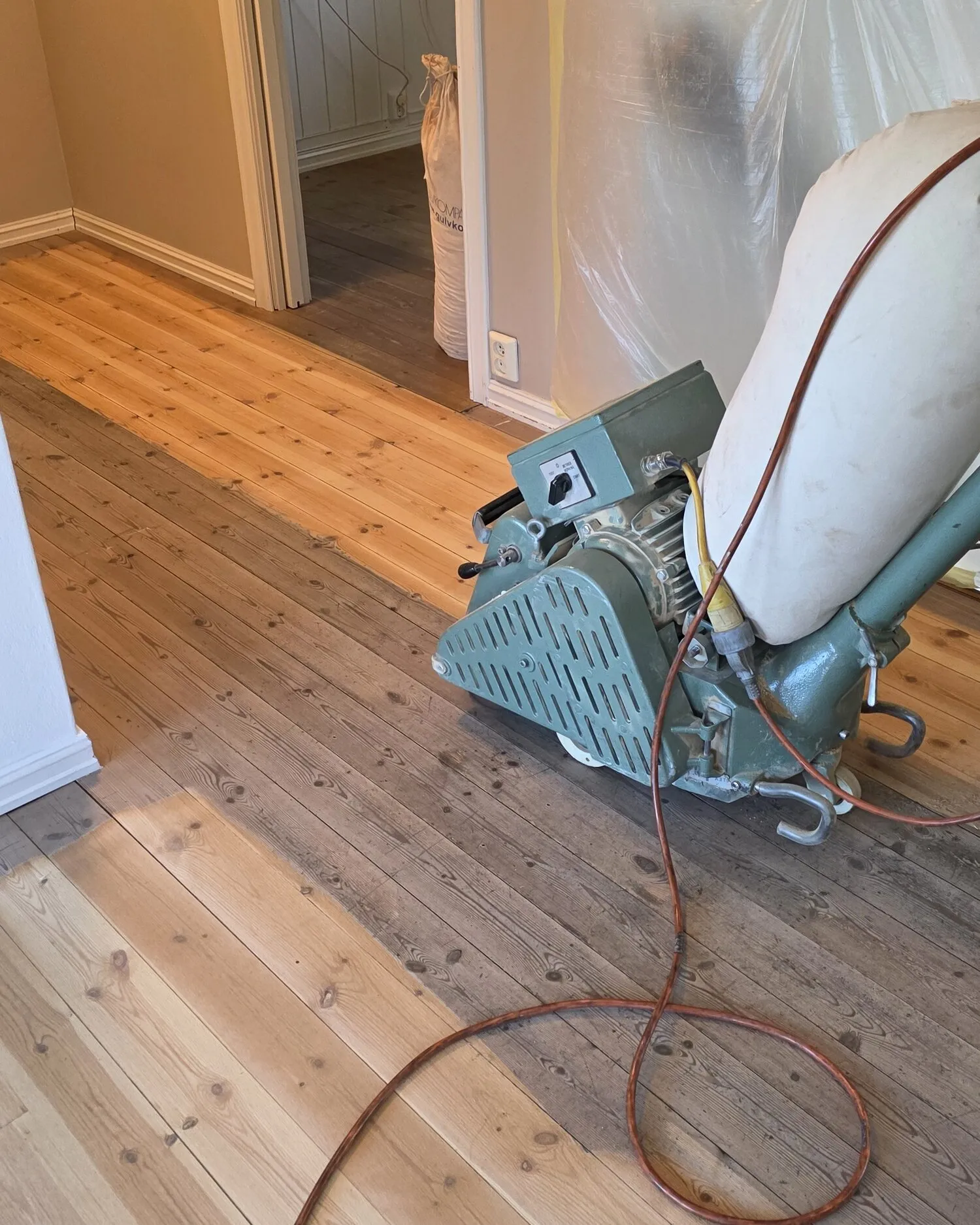 Slipemaskin midt i et rom, med tydelig skille mellom slipt og uslipt gulv